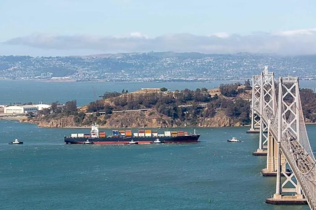 A cargo ship with bridge. surrounding it, crosses under a bridge